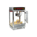 A silver Astro Pop Popcorn Machine with a transparent glass case, open side door, and glowing red POPCORN sign on top. Inside, fresh popcorn fills the bottom beside a stainless steel kettle and two striped popcorn containers.