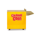 A yellow rectangular cart labeled Caramel Corn in bold red and white letters, featuring a flat metal shelf extending from the right side; this Gold Medal Products cart is on small black wheels and set against a white background.