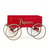 A vintage red Gay 90s Popcorn Wagon with four large gold-spoked wheels and “Popcorn” in ornate gold lettering on the side. The cart, by Gold Medal Products, features a rectangular body and a small wooden handle. The background is plain white.