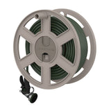 A 100 ft, 5/8 in coiled green garden hose is neatly wound inside a round beige garden hose reel with five wide spokes, mounted on a wall. A black and silver spray nozzle with a green dial hangs below the reel.