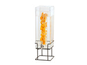 A tall, clear 3 gallon infusion beverage dispenser with a polycarbonate beverage chamber and spigot sits on a black metal stand with an open, geometric design, filled with water and sliced oranges in the central tube.