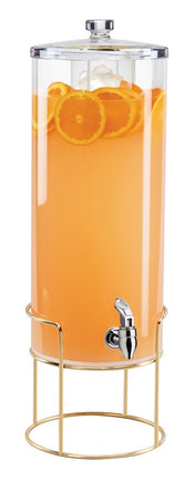 A tall, clear 3 gallon beverage dispenser filled with orange juice and orange slices stands on a gold metal frame, topped with a metal lid. It features a silver spigot near the base for easy pouring and stylish mid-century appeal.