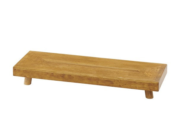 A rectangular Madera Riser with a smooth finish stands on four short, round legs. The visible wood grain and warm, natural brown color highlight its rustic pine charm. The minimalist design is photographed on a white background.