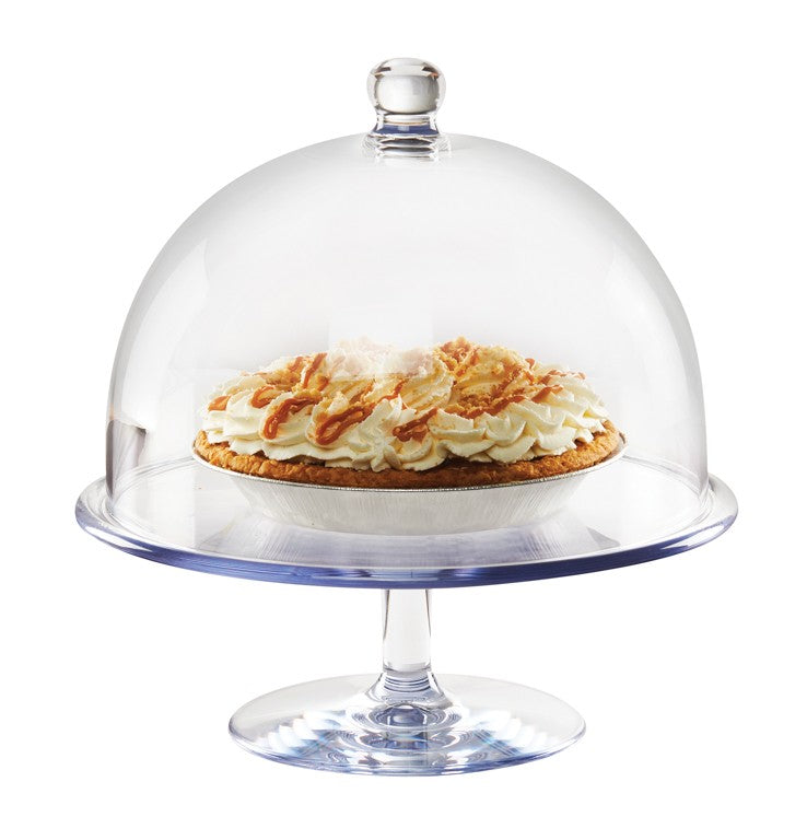 A glass cake stand with a clear polycarbonate dome cover displays a cream-topped pie. The pie has whipped topping and caramelized pieces on a golden crust, with the dome covering most of the pie. The background is plain white.