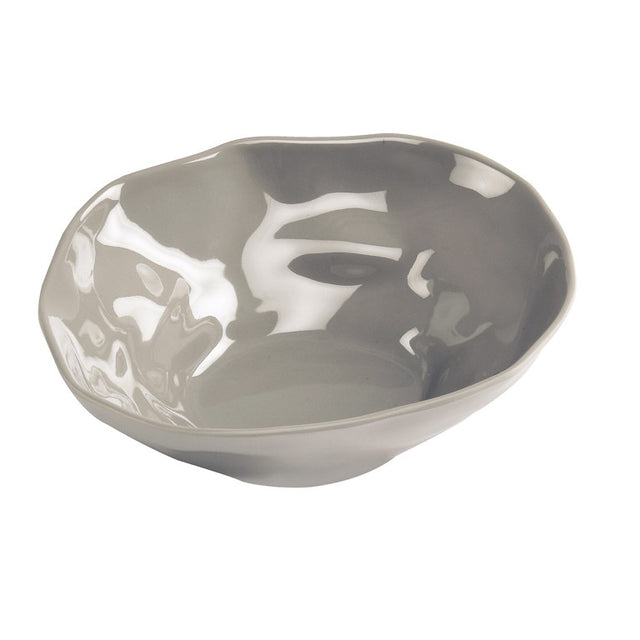A shallow Marin Bowl in ash grey ceramic features an uneven, organic shape and glossy finish. Reflections highlight its smooth, irregular surface and wavy rim, giving this handcrafted bowl a modern look as it sits on a white background.