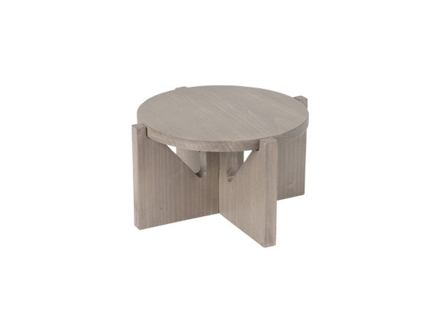 A round, light gray-washed pine wood coffee table with a thick top and a unique crossed-leg base, featuring four wide, flat panels intersecting below the tabletop. The table has a minimalist, modern design and a natural wood grain finish.