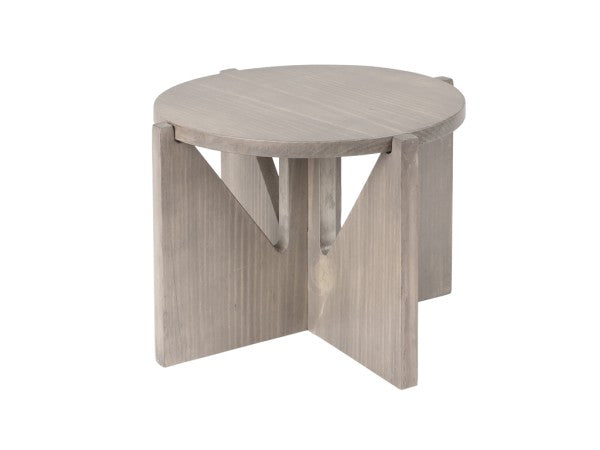 A round, gray-washed pine wood side table with a smooth top and intersecting, flat panel legs forming an X-shape underneath. The knockdown design and minimalist look evoke the modern elegance of the Aspen Riser collection.