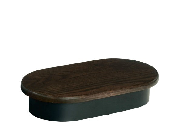 An oval-shaped, dark brown oak Heritage Riser with smooth edges sits atop a black metal base. The object is pictured against a plain white background.