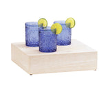Three blue textured drinking glasses, each garnished with a lime wheel on the rim, are arranged on a Newport white-washed pine wood riser against a plain white background.