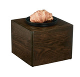 A golden-brown croissant sits on a round black plate, which rests atop a 12" x 12" x 9" Cal-Mil Heritage Riser with visible wood grain, set against a plain white background.