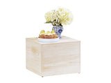 A white-washed pine wood riser holds a blue-patterned vase with white hydrangeas and baby's breath, next to a white plate with three cupcakes topped with lime slices. The background is plain and white.