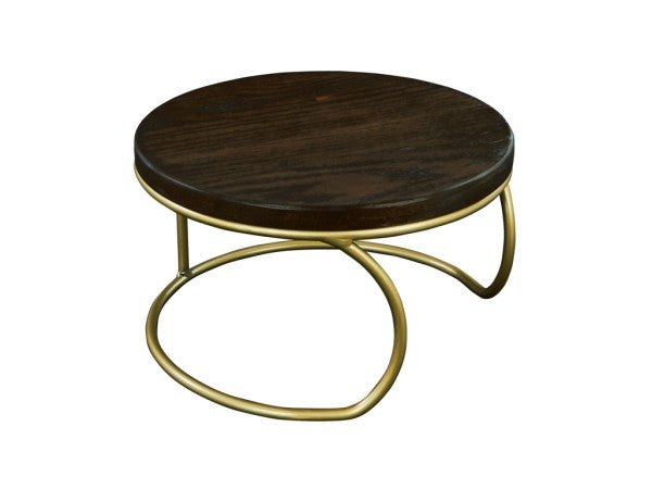 A round Heritage Riser coffee table with a dark stained oak top and a unique matte gold wire base featuring curved, overlapping legs, set against a white background. The modern design contrasts rich wood with the elegant metallic frame.