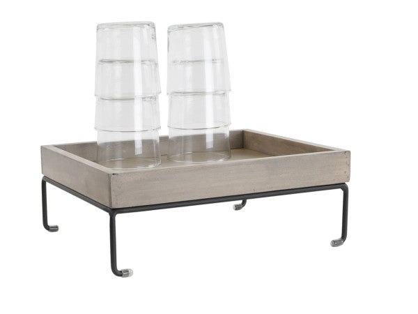 A rectangular wooden tray with a sleek wire frame and black metal legs holds six clear, upside-down drinking glasses stacked in two columns. The minimalist Aspen Riser design by Cal-Mil is showcased against a white background.