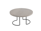 A round, light gray wooden Aspen Riser table with a smooth surface sits on two curved black wire frame metal legs that form open, semi-circular shapes at the base, creating a modern and minimalist Cal-Mil design against a plain white background.