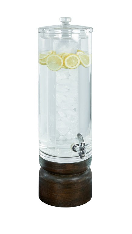 A tall, clear Heritage round beverage dispenser with a metal spigot sits on a dark stained oak base. Filled with water, ice in the center, and floating lemon slices, it’s topped with a glass lid. The background is white.
