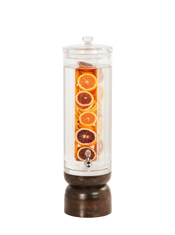 A tall, clear Heritage Beverage Dispenser with a spigot and a sturdy oak base, filled with water and slices of orange, lemon, and blood orange. The citrus slices are stacked vertically inside, gently infusing the water with fresh flavor.