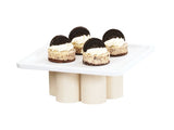 Four mini Oreo cheesecakes with cream topping and an Oreo cookie stand on a modern white cake stand with cylindrical legs and a pine wood riser base, all set against a plain white background.