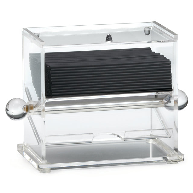 A clear acrylic stir stick dispenser holds a stack of black coffee stirrers. The box features rounded, clear knobs on both sides and an opening at the bottom front for easy access. Its modern, minimalist design complements any space.