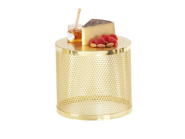 A round, shiny gold metal riser side table with a perforated pattern. On top are a wedge of cheese, a small jar of honey with a dipper, several raspberries, and a few almonds, all neatly arranged. The background is plain white.