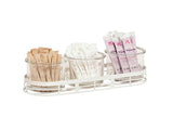 A stainless steel tray holds a neat condiment jar display: three glass jars filled with drink mix packets—tan on the left, white in the center, and purple-and-white on the right—all arranged upright and organized.