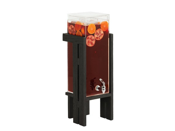 A tall, clear Brooklyn dispenser with a polycarbonate chamber stands on a black wooden base, filled with dark red drink and garnished with whole orange and pomegranate slices. It features a silver spigot and has a transparent lid on top.