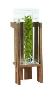 The 3 gallon Sydney Beverage Dispenser features an infusion chamber filled with fresh green mint leaves. This tall, rectangular glass dispenser with a silver spigot sits on a wooden stand against a plain white background.