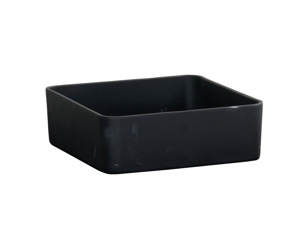 A matte black resin bowl, square-shaped with rounded edges, sits on a white background. The surface shows subtle scuff marks, and the container appears empty.