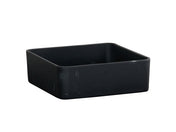 A matte black resin bowl, square-shaped with rounded edges, sits on a white background. The surface shows subtle scuff marks, and the container appears empty.