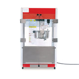 A countertop popcorn maker with a red top, transparent glass sides, an 8 oz kettle inside, and a stainless steel bottom panel. The popcorn machine is plugged in, and operating instructions are visible on a sheet inside the back panel.