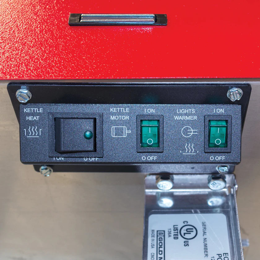 A close-up of a popcorn machine control panel features three labeled switches: “Kettle Heat,” “Kettle Motor,” and “Lights Warmer.” Each switch has on/off positions with indicator lights. The metal panel sits below the 8 oz kettle.