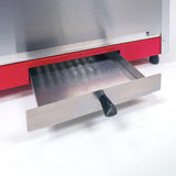 A close-up of a stainless steel countertop popcorn maker with a red accent, showing a metal drip tray partially pulled out. The tray has a black handle and ribbed surface, and the popcorn machine rests on small black feet on a white surface.