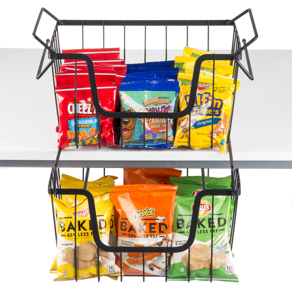 A black powder coated, two-tier metal basket snack rack holds colorful chip and snack bags. The top tier has Cheez-It, Teddy Grahams, and Keebler Elf Grahams; the bottom holds Cheetos Baked and Lay’s Baked. The rack sits on a white table.