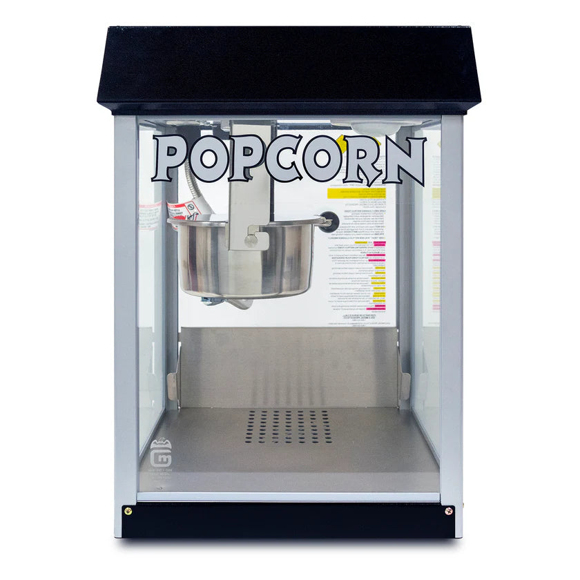 A classic countertop popcorn popper with a black top and glass sides. “POPCORN” is printed in bold letters above a metal popping kettle. The interior is empty, and the base features a perforated metal tray for easy cleanup.