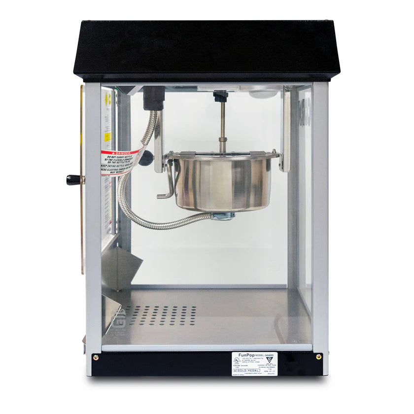 A countertop popcorn machine with a transparent glass body, black top, and stainless steel kettle in the center. The door is closed with no popcorn inside. Control labels and wiring are visible on the left side of this popcorn popper.