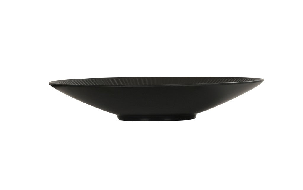A shallow, wide, black ceramic Nomi Bowl with a slightly ribbed texture and a small circular base, photographed on a plain white background. The bowl's minimalist design gives it a modern and elegant appearance.