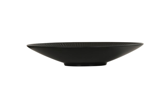 A shallow, wide, black ceramic Nomi Bowl with a slightly ribbed texture and a small circular base, photographed on a plain white background. The bowl's minimalist design gives it a modern and elegant appearance.