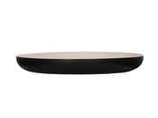 A shallow, round two-tone pasta bowl with a smooth, matte black exterior and a glossy white interior, shown from the side against a white background. The dish has gently curved sides and a flat base.