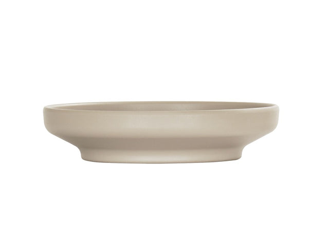 A shallow, round taupe Nova Bowl with a wide coupe rim and smooth matte finish, shown in profile against a plain white background. The bowl has a minimalist design and sits flat on its base.