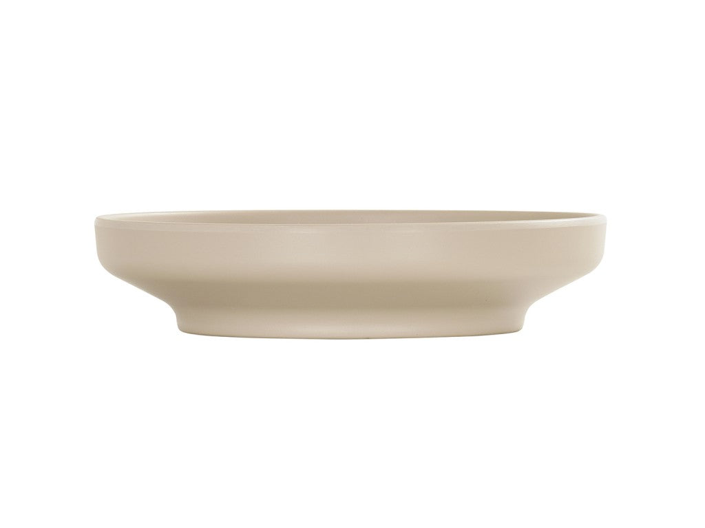 A beige, shallow, round ceramic Nova Bowl with a wide rim and flat base, photographed against a plain white background. This 9 inch bowl features smooth, clean lines and a minimalist design.