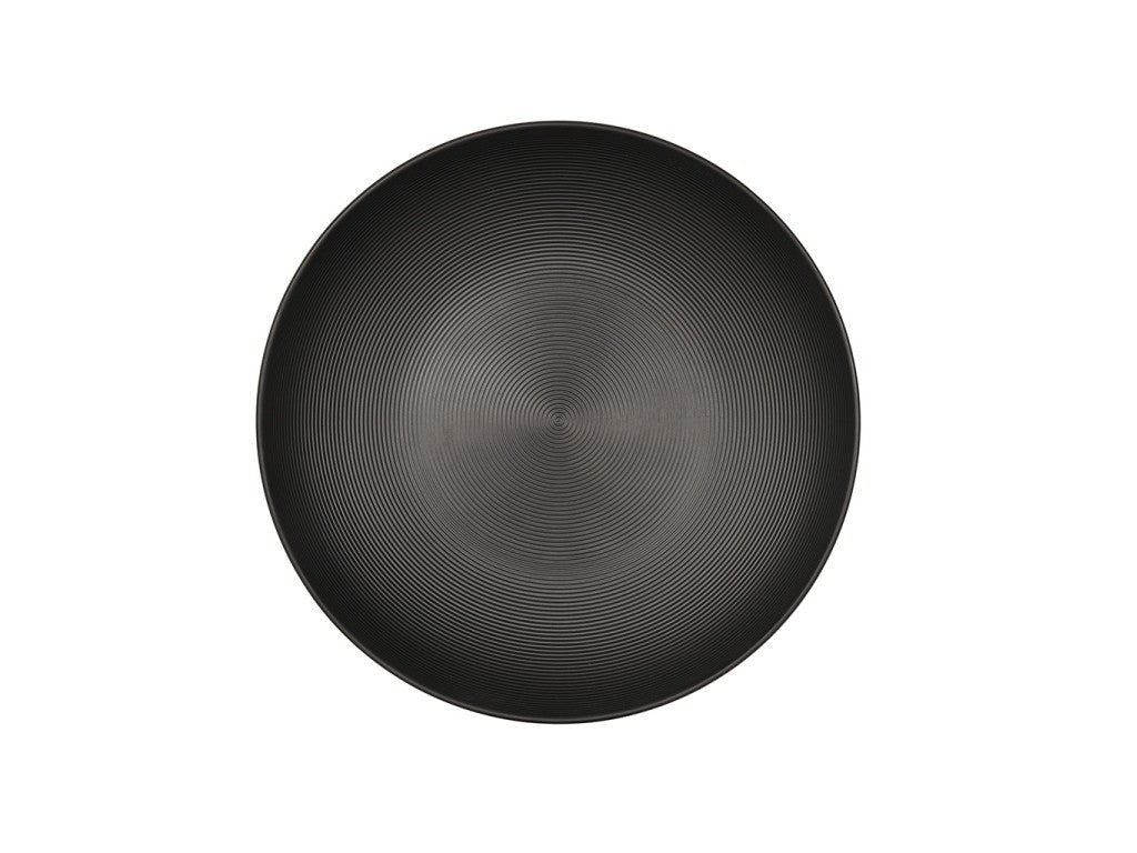 A round, black coupe bowl with a subtle concentric circular pattern radiating from the center, seen from a top-down view against a plain white background. The design creates a sense of texture and depth on the plate’s surface.