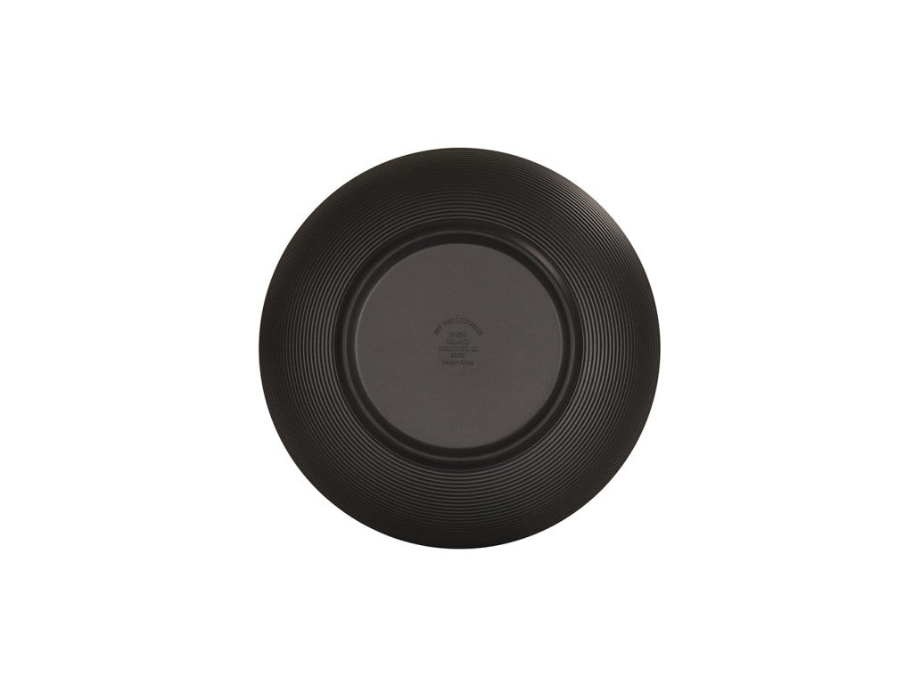 A matte black coupe bowl is shown from above, displaying its circular, ridged design along the rim. The center has indented text with branding and care instructions. The plain white background highlights the Charlotte Bowl’s simple, modern appearance.
