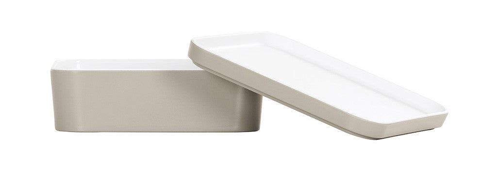 Two rectangular white ceramic containers, reminiscent of a Bento Box, are shown; one lies flat while the other stands diagonally, partially overlapping. Both feature smooth surfaces and rounded edges, displayed elegantly on a white background.