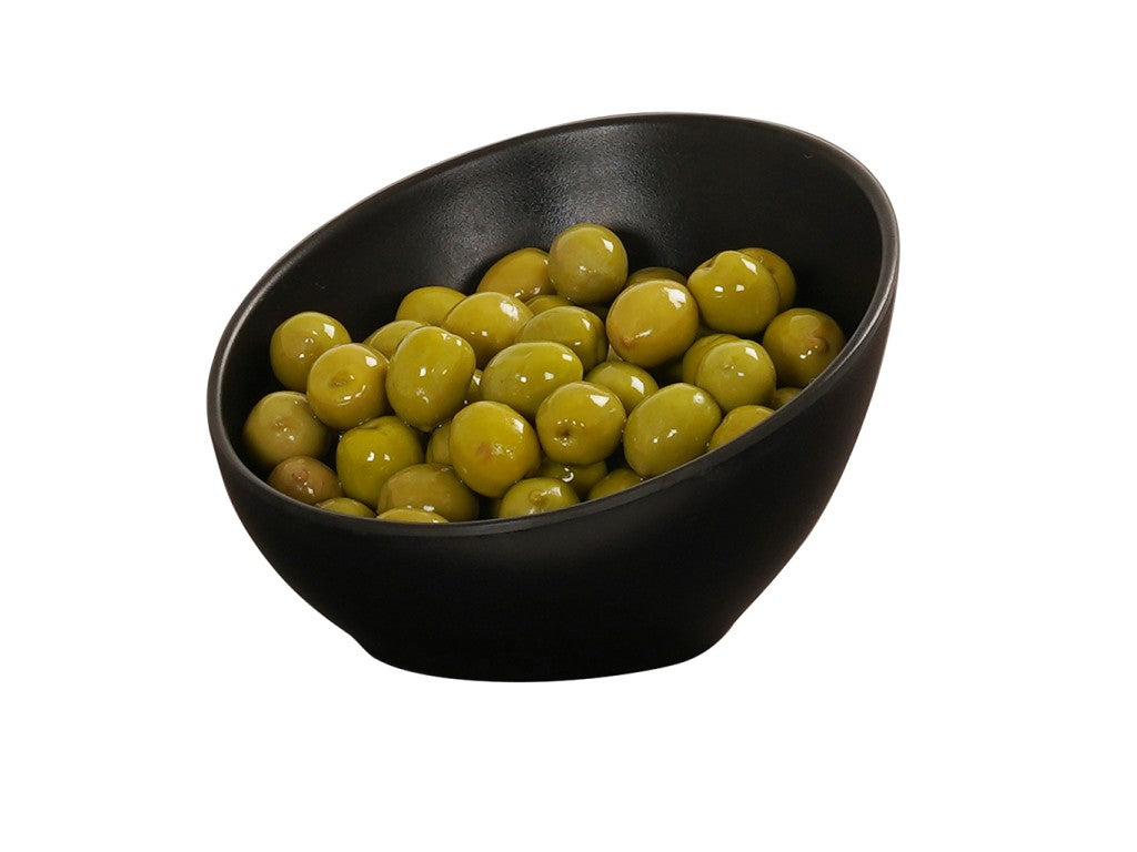 A matte black bowl, slightly tilted, is filled with shiny green olives against a plain white background. The simple bowl’s smooth surface emphasizes the vibrant color of the glistening olives coated in oil or brine.