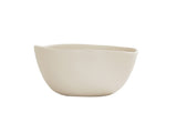 A cream-colored, smooth Bali Soup Bowl with asymmetrical, gently curved edges sits on a plain white background. This minimalist ceramic bowl features a matte finish and is dishwasher safe for easy cleaning.