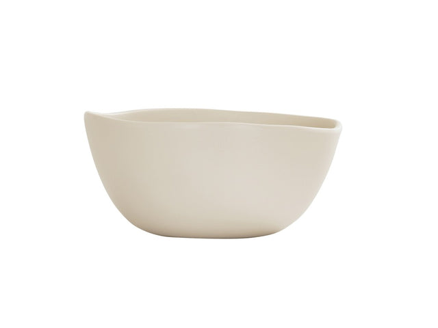 A cream-colored, smooth Bali Soup Bowl with asymmetrical, gently curved edges sits on a plain white background. This minimalist ceramic bowl features a matte finish and is dishwasher safe for easy cleaning.