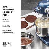 A blue Luna Planetary Mixer with a metal bowl filled with whipped mixture sits next to two round chocolate cake layers, a plate of chocolate batter, and a spatula on a stainless steel counter. Text on the left lists the mixer’s uses and certification logos appear below.