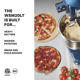 A blue Luna Planetary Mixer with a dough hook and dough in the bowl sits beside two baked pizzas on a gray surface. Fresh tomatoes, basil, and a pizza cutter complete the scene. Text highlights its uses for heavy batters and pizza or bread doughs.