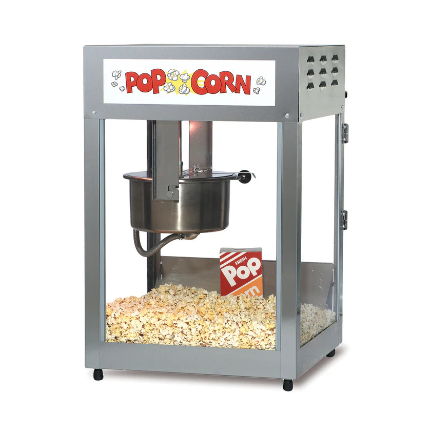 A metal countertop popcorn maker with glass sides and a Pop Corn sign at the top. Inside, a stainless steel kettle pops fresh popcorn, with a red-and-white striped popcorn box sitting atop the golden pile.