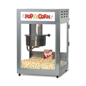 A metal countertop popcorn maker with glass sides and a Pop Corn sign at the top. Inside, a stainless steel kettle pops fresh popcorn, with a red-and-white striped popcorn box sitting atop the golden pile.