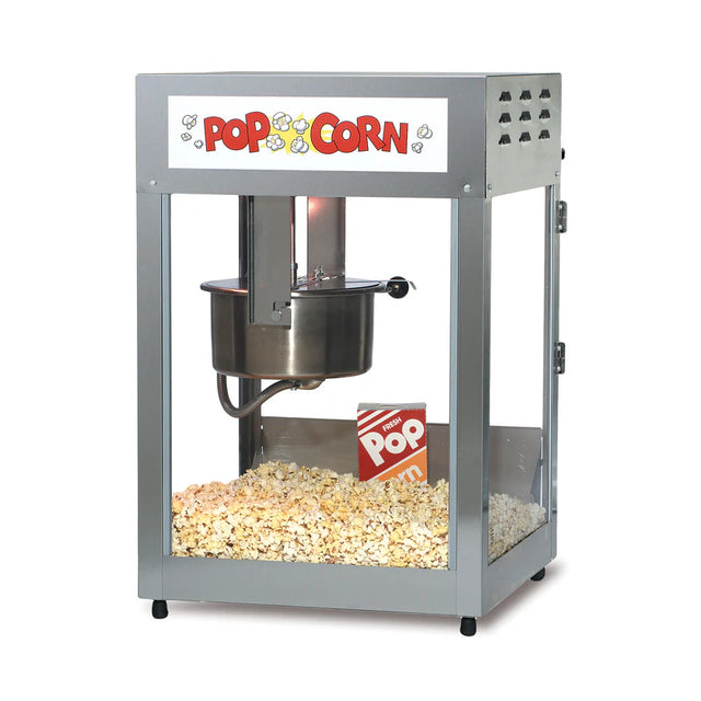 A metal countertop popcorn maker with glass sides and a Pop Corn sign at the top. Inside, a stainless steel kettle pops fresh popcorn, with a red-and-white striped popcorn box sitting atop the golden pile.